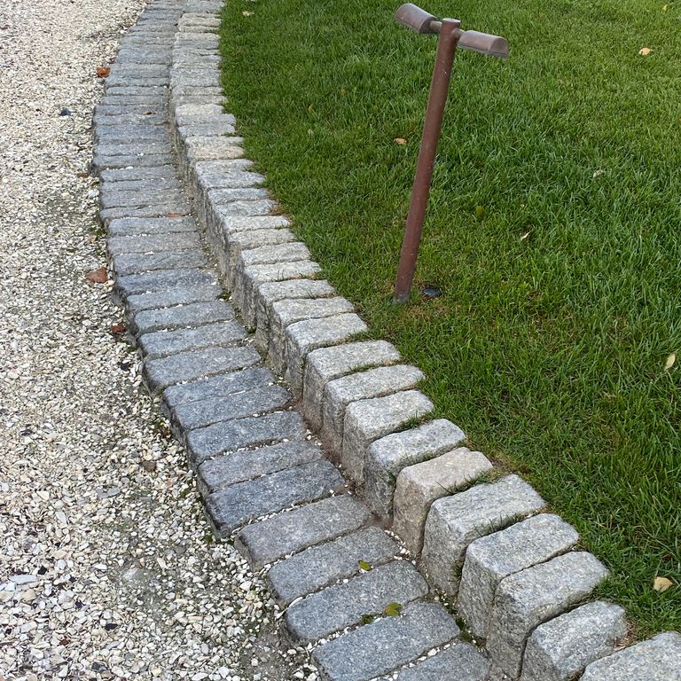 Application image for Gray Granite Cobblestone - Rectangles. The image shows this product being used in a landscape curbing & edging application. The surface finish shown is tumbled. The dominant color shown is gray; with blue, green and white secondaries. The color mix creates a cool feeling. Speckled and coarse speckled color patterns. Contains some mica and mineral inclusions.