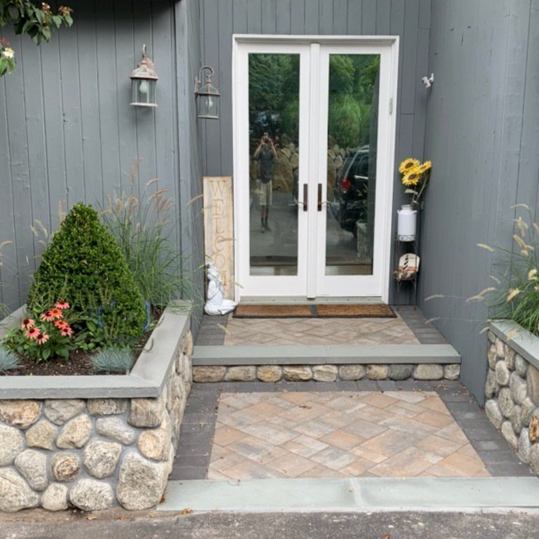 Application image for Cedar Creek River Rounds - Thin Veneer. The image shows this product being used in a landscape wallstone application. The surface finish shown is natural. Dominant colors shown are beige, gray and tan; with brown and cream secondaries. The color mix creates a warm feeling. Regular color pattern.