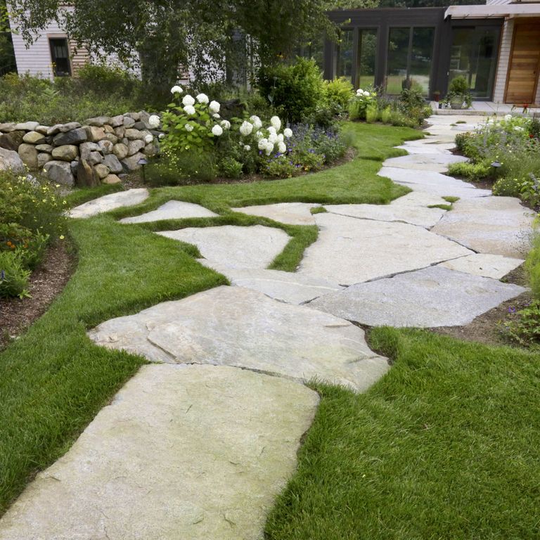 Application image for Dodlin Hill Irregular Flagstone. The image shows this product being used in a path pavers application. The surface finish shown is a combination of natural cleft and weathered. Dominant colors shown are beige and gray; with white, tan and cream secondaries. Exhibits 