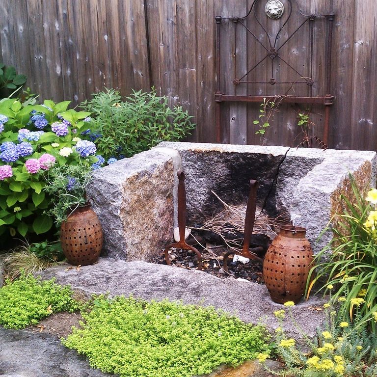 Application image for Reclaimed Granite Curbstone Fire Feature. The image shows this product being used in an outdoor fire concepts application. The surface finish shown is a combination of split-face with flat plane, weathered and worn. The dominant color shown is gray; with beige, orange/rust, white and tan secondaries. The color mix creates a warm feeling.