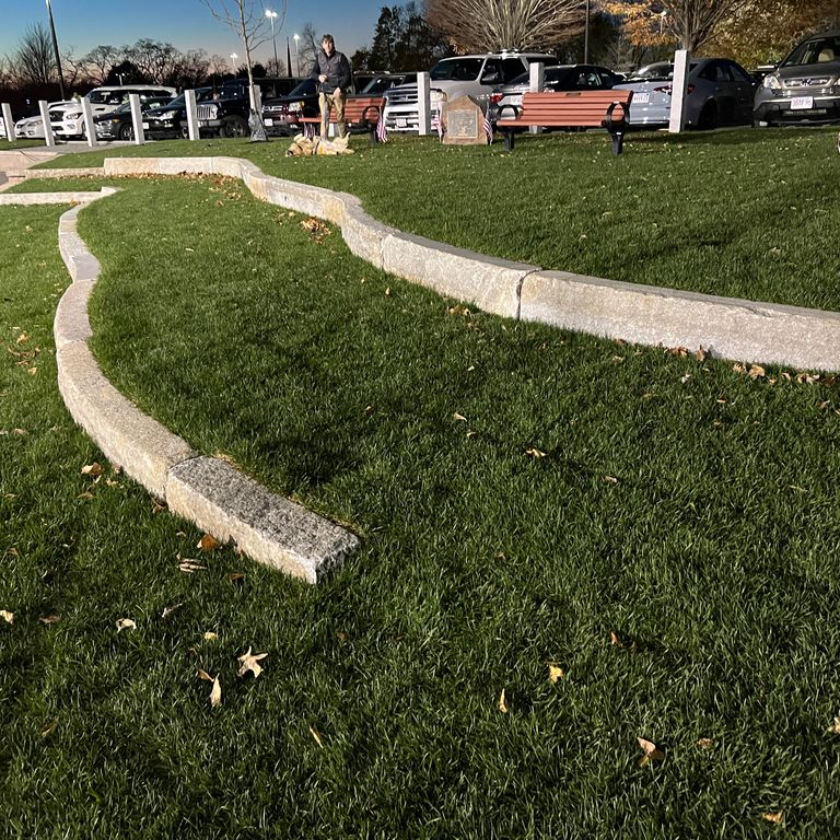 Application image for Reclaimed Third Generation Granite Curbstone - Lawn Steps. The image shows this product being used in a landscape curbing & edging application. The surface finish shown is . Dominant colors shown are gray and tan. The color mix creates a warm feeling. Regular color pattern.