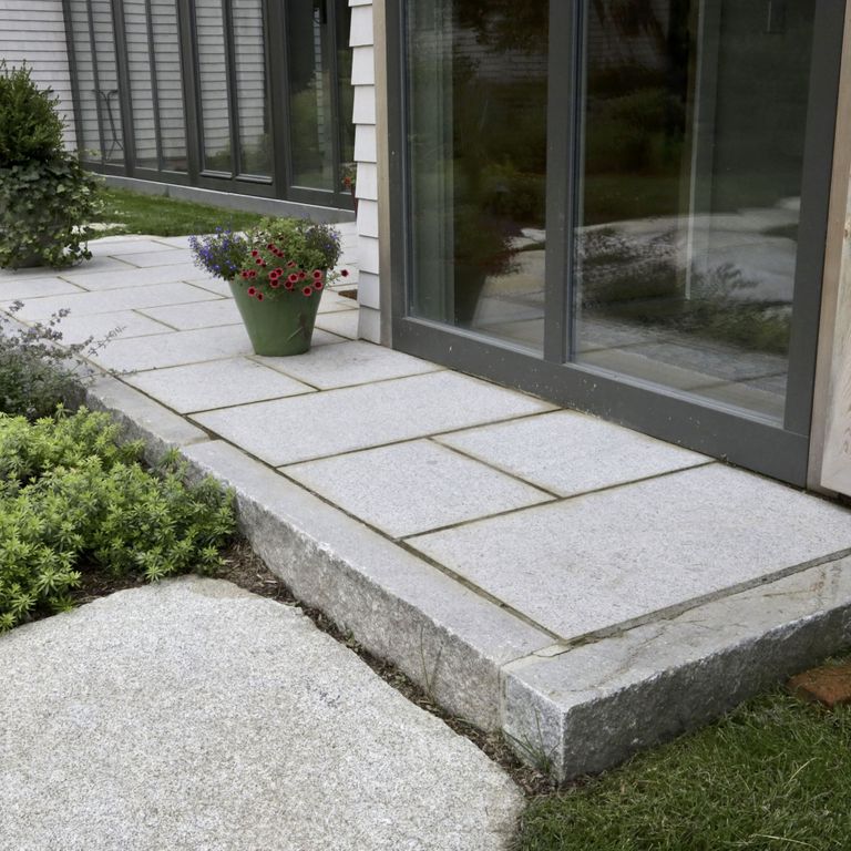Feature image for Reclaimed Third Generation Granite Curbstone Edging. The image shows this product being used in a landscape curbing & edging application. Dominant colors shown are gray and white; with beige and orange/rust secondaries. The color mix creates a cool feeling. Speckled and blotched color patterns.