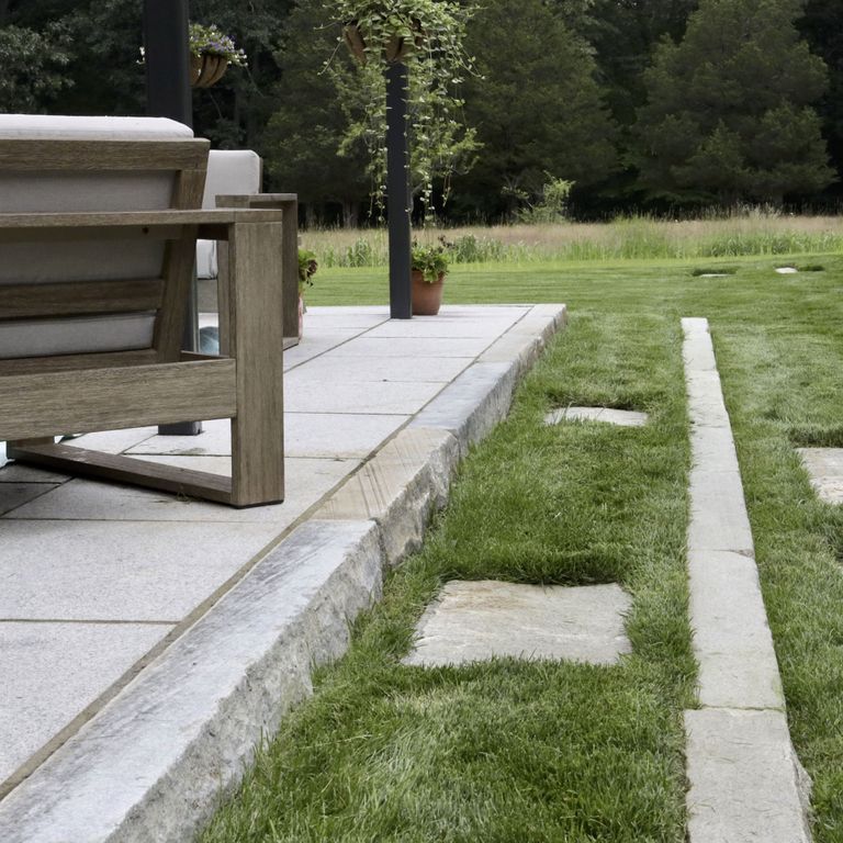 Application image for Reclaimed Third Generation Granite Curbstone Edging. The image shows this product being used for landscape curbing & edging and monolithic steps. The surface finish shown is a combination of sawn, split-face with flat plane, weathered and worn. Dominant colors shown are gray and white; with beige and blue secondaries. The color mix creates a cool feeling. Fine speckled color pattern.