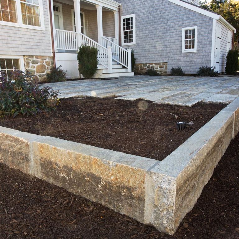 Application image for Reclaimed Third Generation Granite Curbstone Edging. The image shows this product being used in a landscape curbing & edging application. The surface finish shown is a combination of sawn, split-face with flat plane, weathered and worn. Dominant colors shown are brown, gray and tan; with beige, orange/rust and white secondaries. The color mix creates a warm feeling. Speckled and blotched color patterns.
