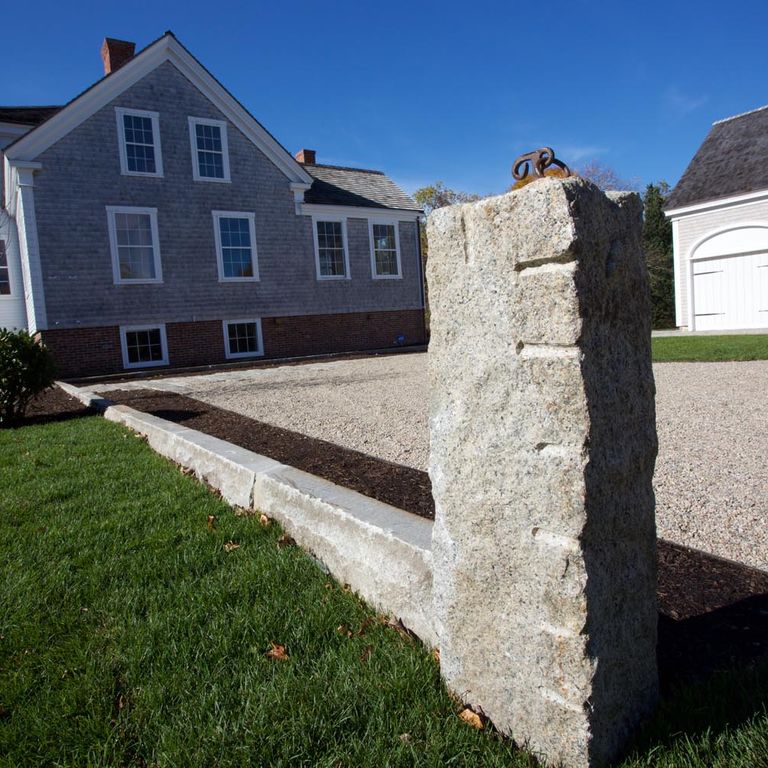 Application image for Reclaimed Third Generation Granite Curbstone Edging. The image shows this product being used in a landscape curbing & edging application. The surface finish shown is a combination of sawn, split-face with flat plane, weathered and worn. Dominant colors shown are beige and gray; with white and cream secondaries. The color mix creates a cool feeling. Fine speckled and blotched color patterns.