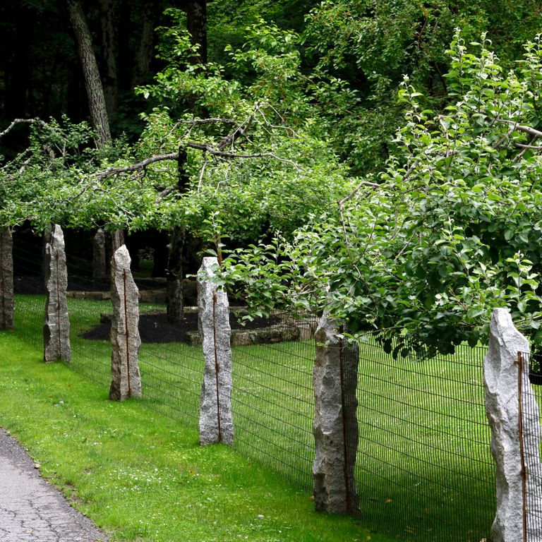 Application image for Reclaimed First Generation Curbstone - Posts. The image shows this product being used in a posts application. The surface finish shown is split-face with rough plane. The dominant color shown is gray; with black, brown and white secondaries. The color mix creates a cool feeling. Speckled and blotched color patterns.
