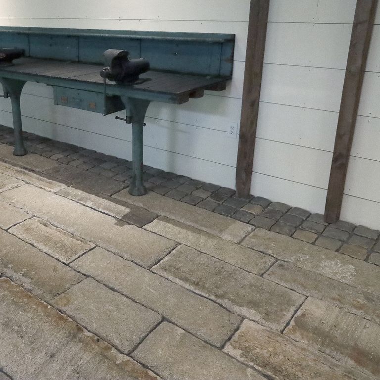 Application image for Reclaimed First Generation Granite Curbstone - Gauged Floor Planks. The image shows this product being used in an interior floor application. The surface finish shown is a combination of split-face with flat plane, weathered and worn. Dominant colors shown are brown and gray; with beige, orange/rust, purple and tan secondaries. The color mix creates a warm feeling. Regular and blotched color patterns.
