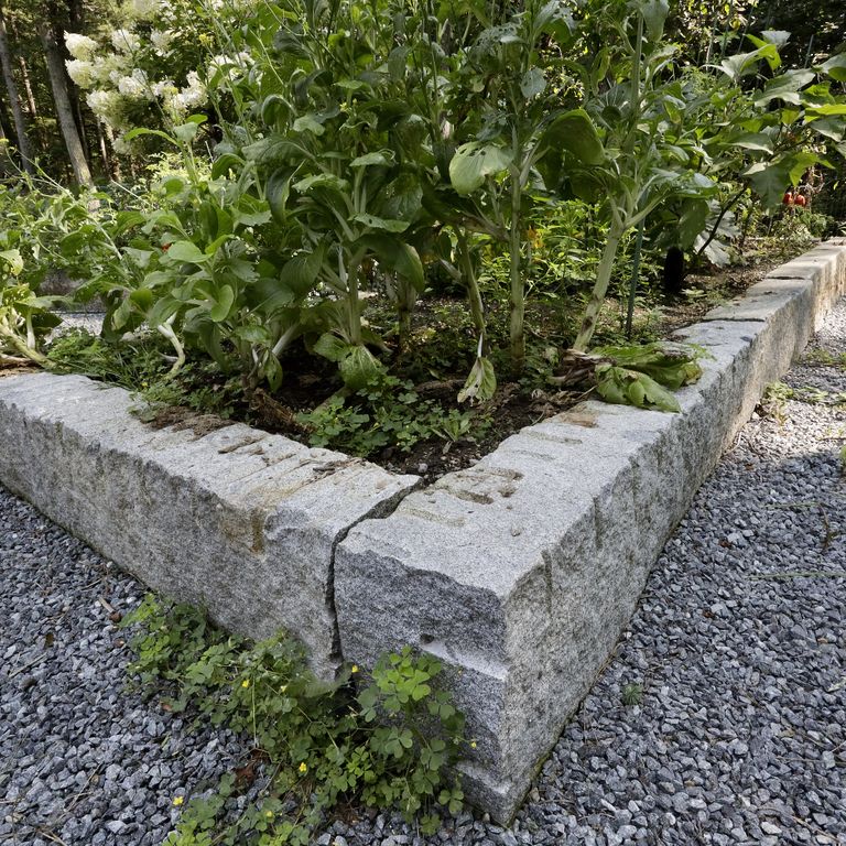 Application image for Reclaimed Granite Curbstone Garden Accents. The image shows this product being used in a garden accents application. The surface finish shown is a combination of chiseled, split-face, weathered and worn. The dominant color shown is gray; with blue, brown, orange/rust and tan secondaries. The color mix creates a warm feeling. Speckled color pattern.