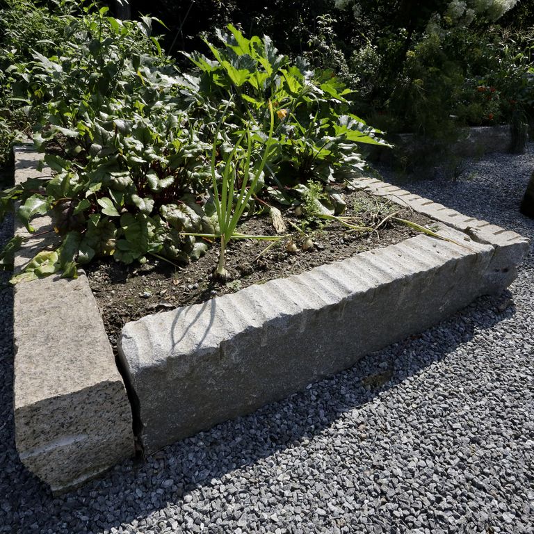 Application image for Reclaimed Granite Curbstone Garden Accents. The image shows this product being used in a garden accents application. The surface finish shown is a combination of chiseled, split-face, weathered and worn. The dominant color shown is gray; with beige, blue and brown secondaries. The color mix creates a warm feeling. Speckled color pattern.