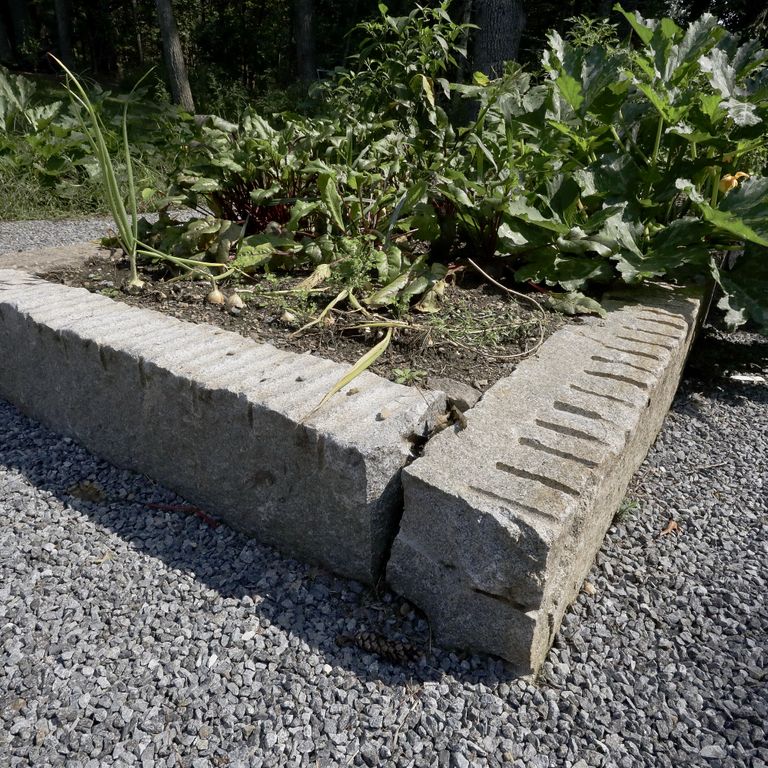 Application image for Reclaimed Granite Curbstone Garden Accents. The image shows this product being used in a garden accents application. The surface finish shown is a combination of chiseled, split-face with flat plane, weathered and worn. The dominant color shown is gray; with beige, blue, brown and white secondaries. The color mix creates a warm feeling. Speckled color pattern.