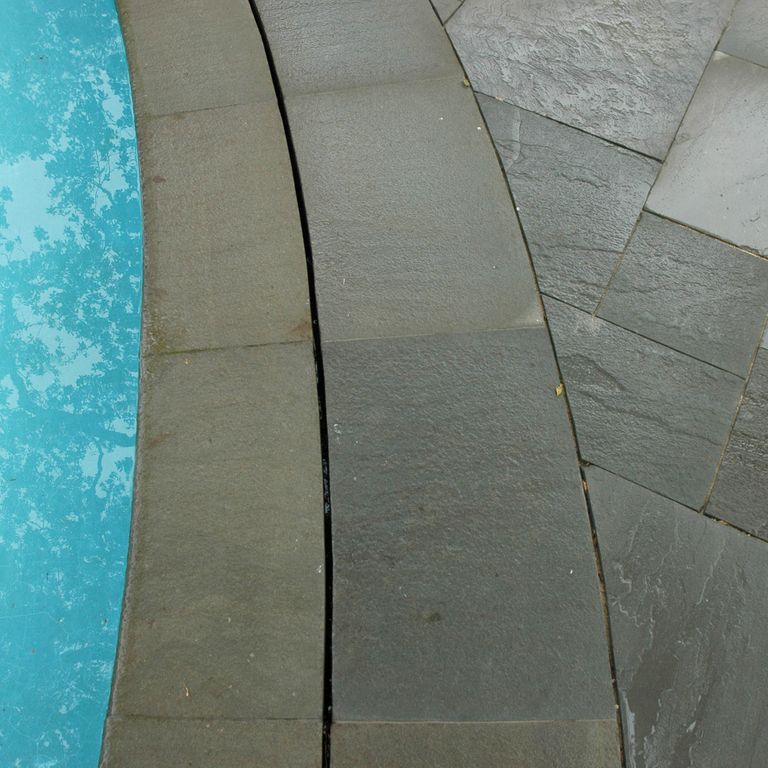 Best close-up image for Bluestone Natural Cleft Green/Brown - Pool Coping. The image shows this product being used for pool coping and patio pavers. The surface finish shown is natural cleft. Dominant colors shown are green and gray; with a brown secondary. The color mix creates a cool feeling. Solid and regular color patterns.
