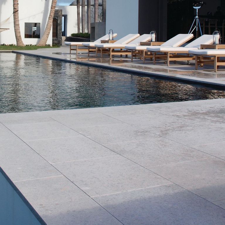 Best close-up image for Classimo Sky Limestone - Pool Deck. The image shows this product being used in a pool deck pavers application. The surface finish shown is sand blasted. Dominant colors shown are gray and white; with a blue secondary. The color mix creates a cool feeling. Regular and cloudy color patterns.