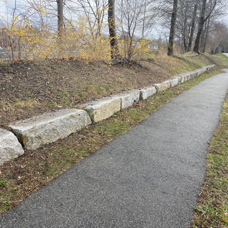 Application image for Reclaimed Granite Block - Edging. The image shows this product being used in a landscape curbing & edging application. The surface finish shown is a combination of split-face and weathered. The dominant color shown is gray; with beige, white, tan and cream secondaries. The color mix creates a warm feeling. Speckled color pattern.