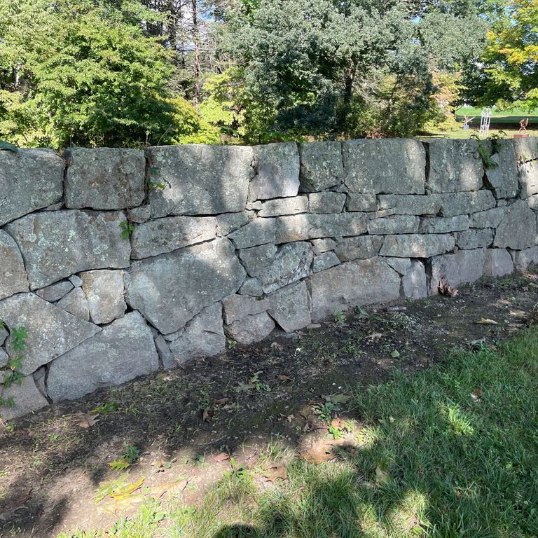 Application image for New England Fieldstone Mix - Oversized Wallstone. The image shows this product being used in a landscape wallstone application. The surface finish shown is weathered. The dominant color shown is gray; with a brown secondary. The color mix creates a cool feeling. Regular and blotched color patterns.