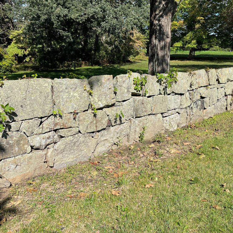 Application image for New England Fieldstone Mix - Oversized Wallstone. The image shows this product being used in a landscape wallstone application. The surface finish shown is weathered. Dominant colors shown are beige and tan; with brown, gray and cream secondaries. The color mix creates a warm feeling. Regular and speckled color patterns.