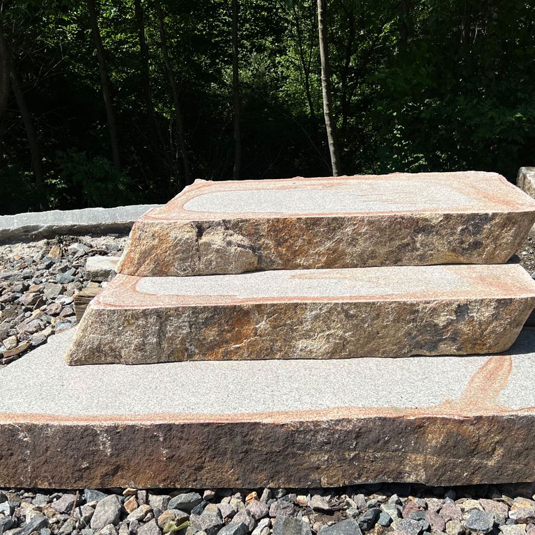 Feature image for Cape Neddick Granite Full Color - Live Edge Steps - Flamed Tops. The image shows this product being used in a monolithic steps application. The surface finish shown is a combination of flamed and natural. Dominant colors shown are beige, black, brown, gray and tan; with blue, orange/rust, purple, white and cream secondaries. The color mix creates a warm feeling. Speckled and blotched color patterns.