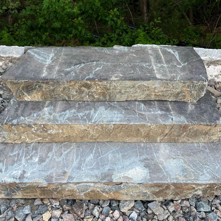Application image for Granite - Mystic Mountain - Live Edge Steps - Flamed Tops. The image shows this product being used in a monolithic steps application. The surface finish shown is a combination of flamed and natural. Dominant colors shown are blue and gray; with beige, brown, green, orange/rust, white and tan secondaries. Exhibits 