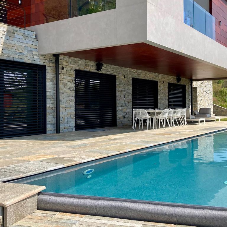 Application image for Pietra Italia Full Color Gneiss - Pool Coping. The image shows this product being used for pool coping and pool deck pavers. The surface finish shown is natural cleft. Dominant colors shown are beige and tan; with brown, gray, orange/rust and cream secondaries. Exhibits 