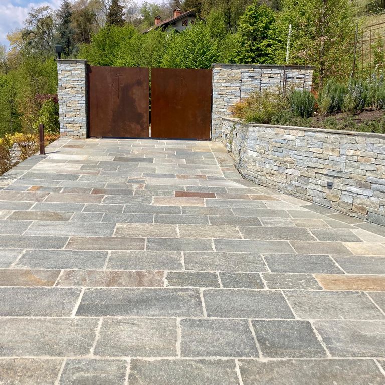 Feature image for Pietra Italia Full Color Gneiss - Pavers. The image shows this product being used in a driveway pavers application. The surface finish shown is natural cleft. Dominant colors shown are beige and gray; with brown, green, orange/rust, pink, purple, white, tan and cream secondaries. The color mix creates a warm feeling. Regular, linear and random color patterns.