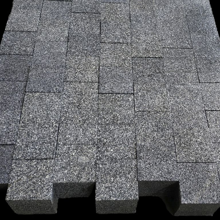 Feature image for Tai Black Granite Cobblestones. The surface finish shown is a combination of flamed and sawn. The dominant color shown is gray. The color mix creates a cool feeling. Regular and speckled color patterns.