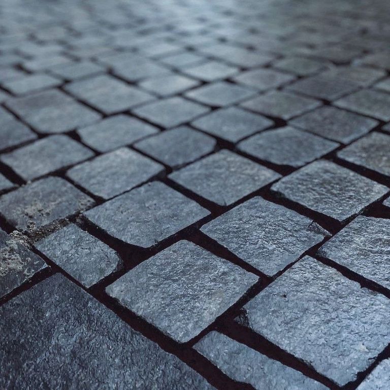 Application image for Basalt - Black Moon - Cobblestone. The image shows this product being used in a patio pavers application. Dominant colors shown are black, blue and gray. The color mix creates a cool feeling.