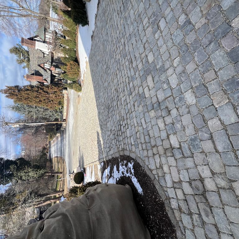 Feature image for Reclaimed European Porphyry Cobblestones - Square - Worn Surface. The image shows this product being used in a driveway pavers application. The surface finish shown is . The dominant color shown is gray. The color mix creates a cool feeling.