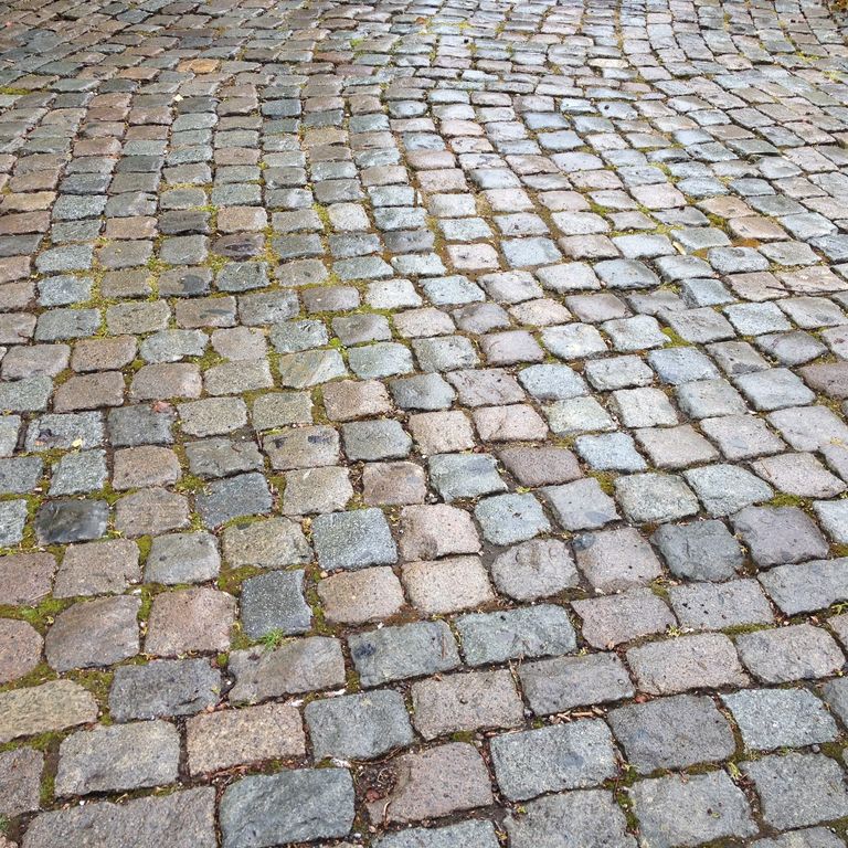 Application image for Reclaimed European Porphyry Cobblestones - Square - Antiqued. The image shows this product being used in a driveway pavers application. The surface finish shown is . The dominant color shown is gray. The color mix creates a warm feeling.