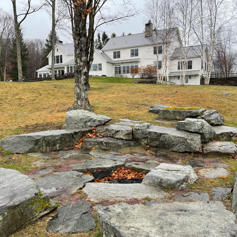 Application image for New England Fieldstone Boulders & Ledgestone - Seating & Benches. The image shows this product being used for outdoor fire concepts, garden accents, seating & benches and monolithic steps. The surface finish shown is weathered. The dominant color shown is gray; with green and white secondaries. The color mix creates a cool feeling. Regular and random color patterns.