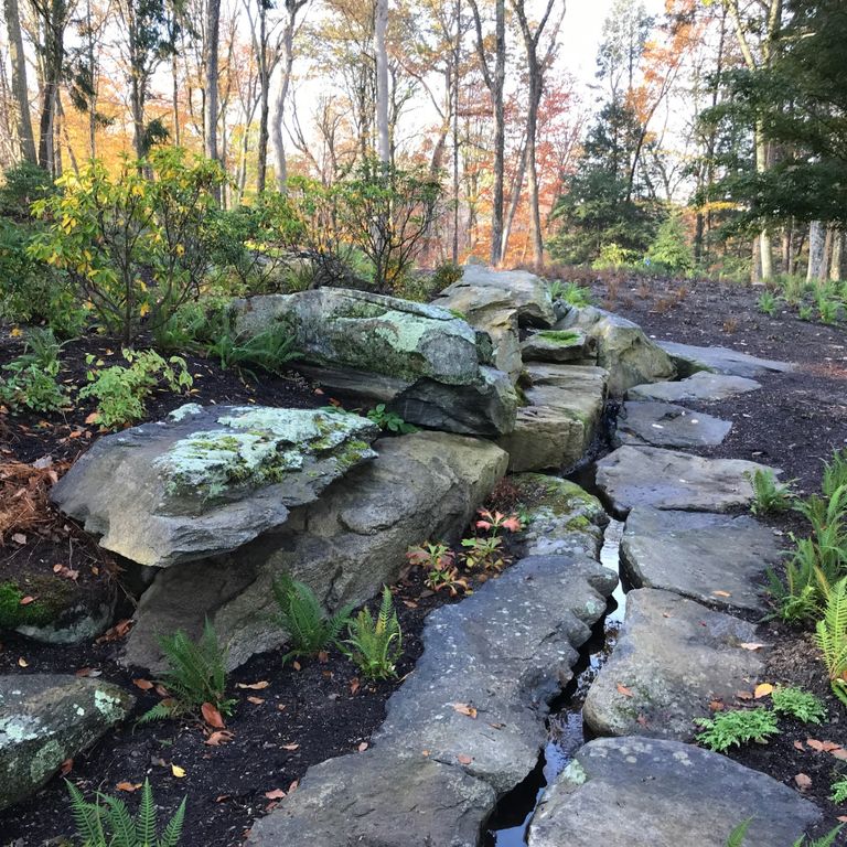 Application image for New England Fieldstone Boulders & Ledgestone - Pool/Pond Coping. The image shows this product being used for water features and landscape boulders & ledge. The surface finish shown is weathered. The dominant color shown is gray; with black, blue, green and white secondaries. The color mix creates a cool feeling. Regular and blotched color patterns.
