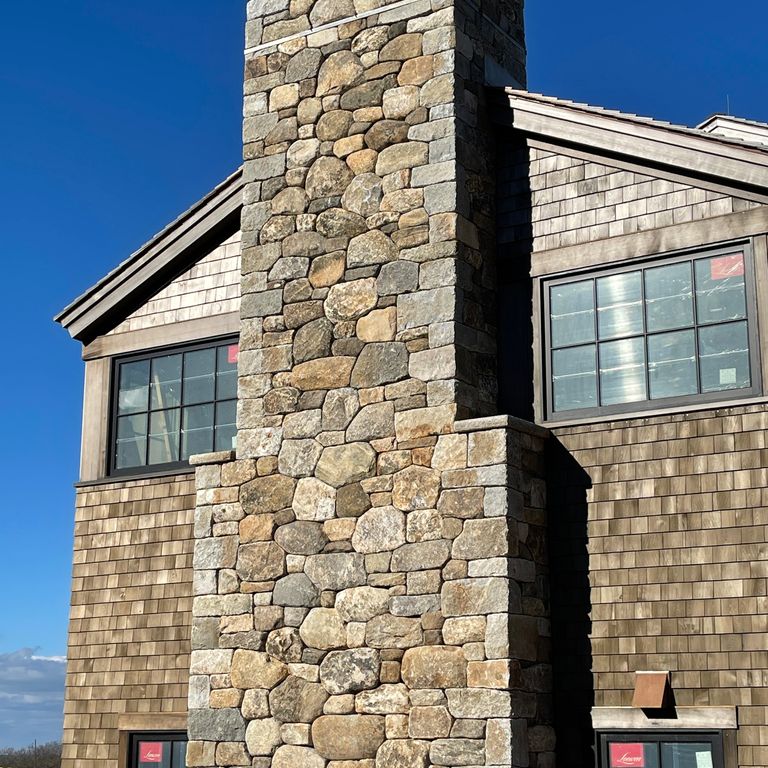 Application image for New England Fieldstone Mix - Veneer. The image shows this product being used in a full bed veneer application. The surface finish shown is weathered. Dominant colors shown are brown, gray and tan.