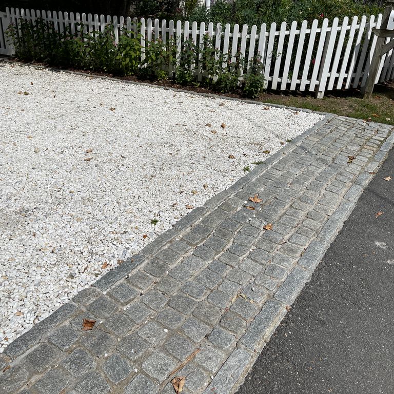 Application image for Gray Granite Cobblestone - Squares. The image shows this product being used in a driveway aprons application. The surface finish shown is tumbled. The dominant color shown is gray; with a brown secondary. The color mix creates a cool feeling. Speckled color pattern. Contains some mica and mineral inclusions.