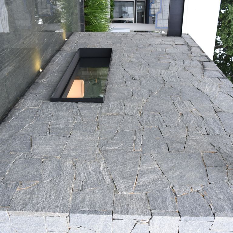 Feature image for Brazilian Lucerna Gneiss - Veneer. The image shows this product being used in a full bed veneer application. The surface finish shown is split-face. The dominant color shown is gray. The color mix creates a cool feeling.