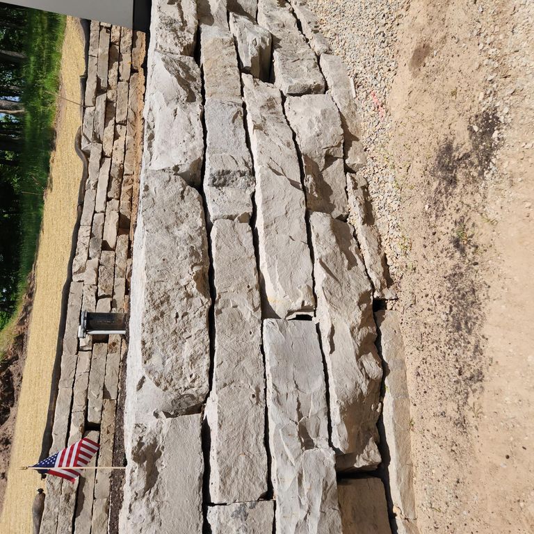 Application image for Lannon Gray Limestone - Wallstone. The image shows this product being used for landscape wallstone and retaining wall. The surface finish shown is natural cleft. The dominant color shown is gray. The color mix creates a warm feeling.