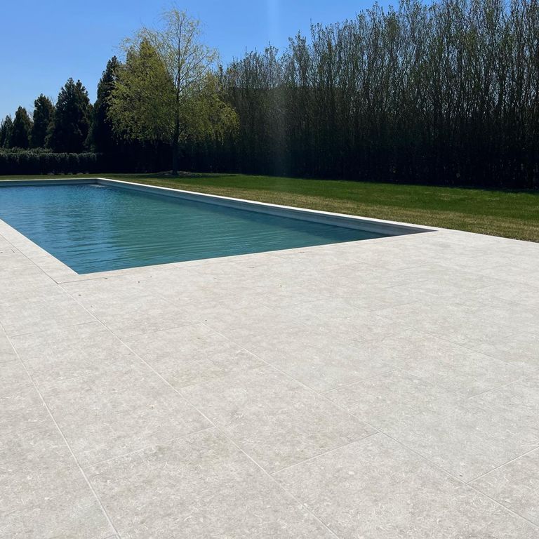 Application image for Veneto Olivo Limestone - Pool Coping. The image shows this product being used for pool coping and pool deck pavers. The surface finish shown is flamed. The dominant color shown is gray. The color mix creates a warm feeling.